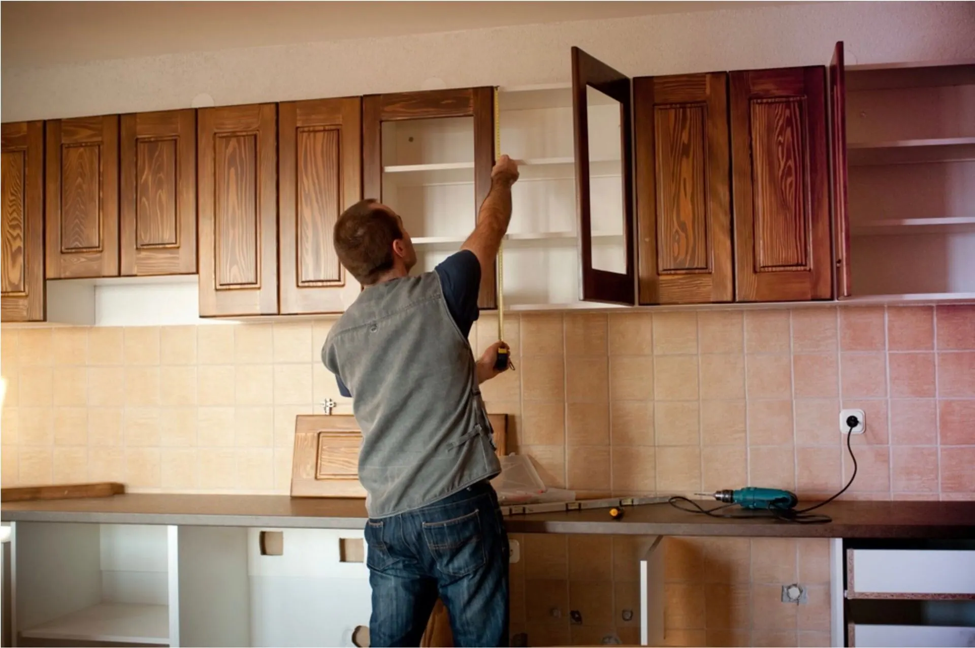 Man installing kitchen cabinets with a measuring tape. Cabinets are wooden. Interior.