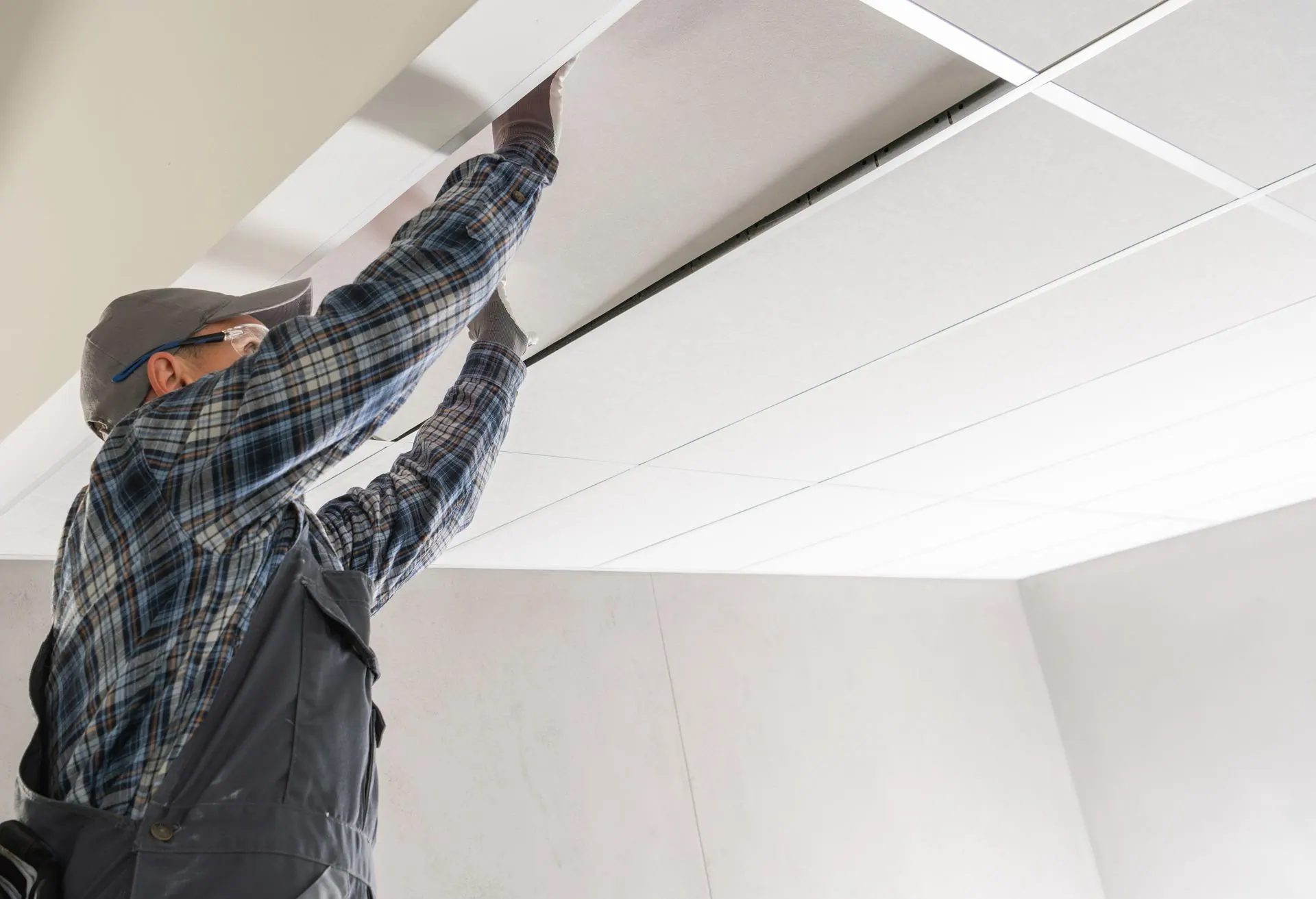 A man is hanging a tile ceiling in a room.