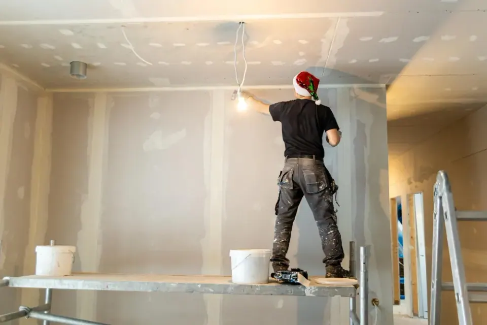 Person in Santa hat, on scaffold, working on drywall in a room under construction.