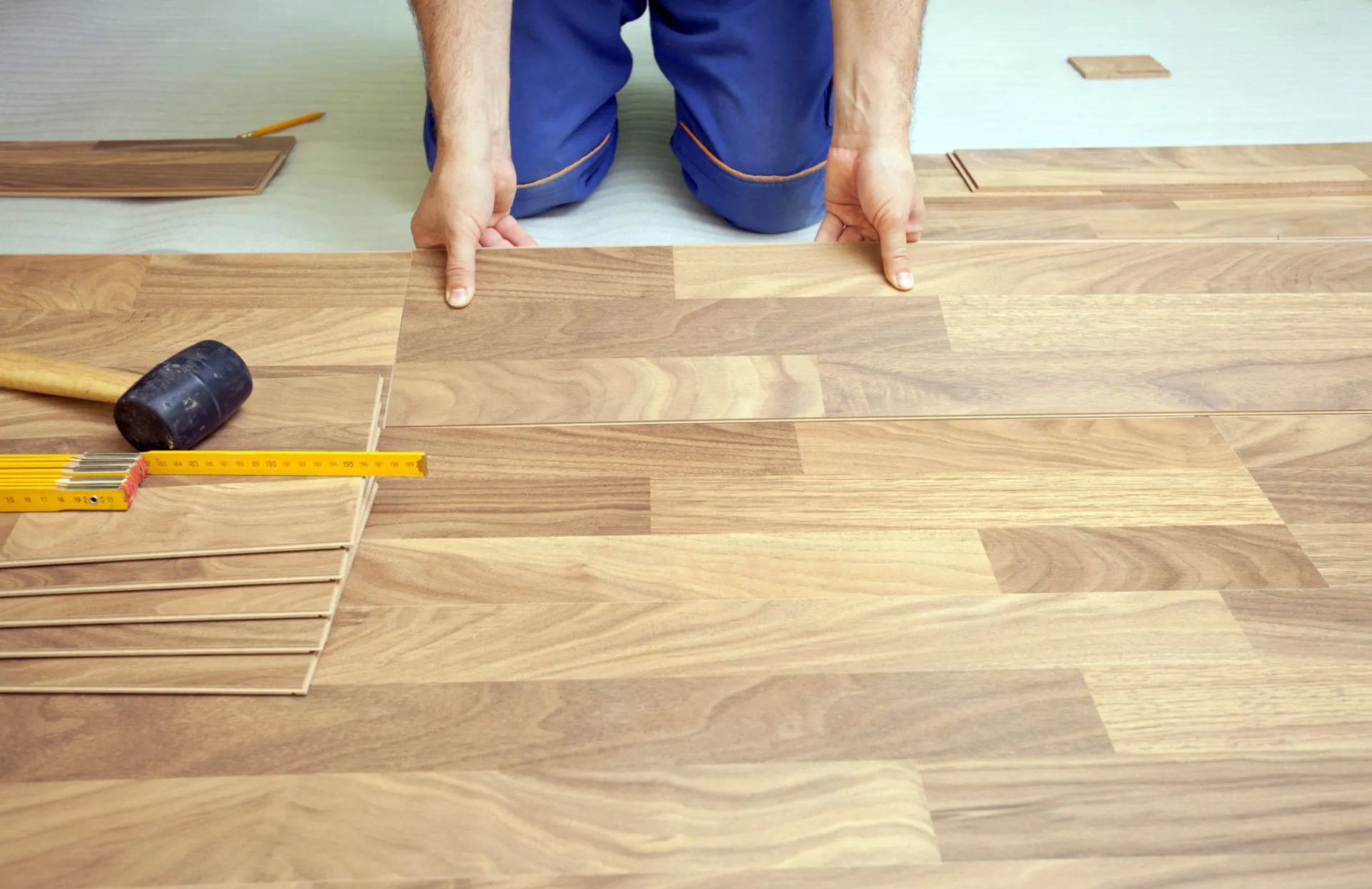 A man is kneeling down to install a wooden floor.