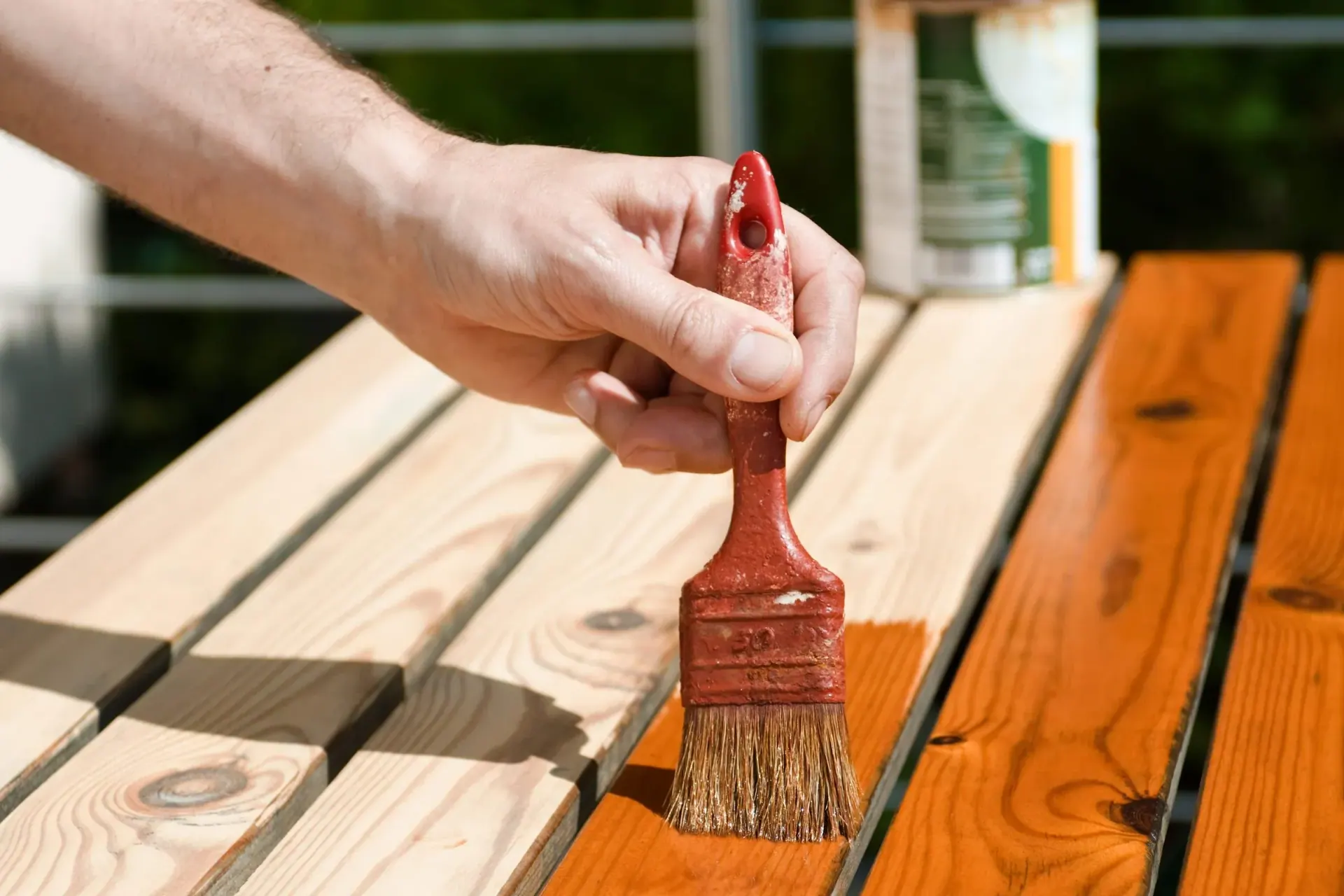 Hand varnishing a wooden table with a brush, highlighting the contrast between unfinished and finished wood.