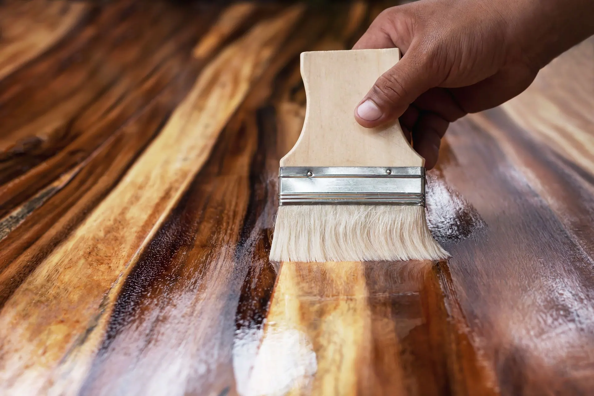 Hand applying varnish to a wood surface with a brush, creating a glossy, wet finish.