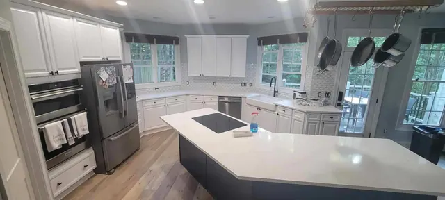 Wide corner view of a renovated kitchen with a navy blue island, white cabinets, and hexagon tile backsplash.
