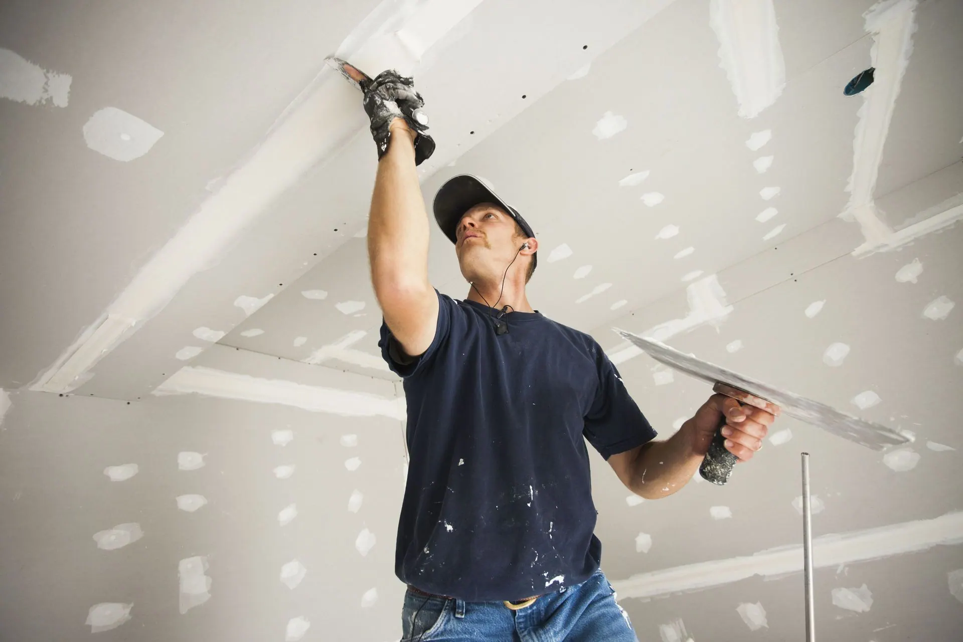 A worker skim-coating a drywall ceiling with a taping knife.