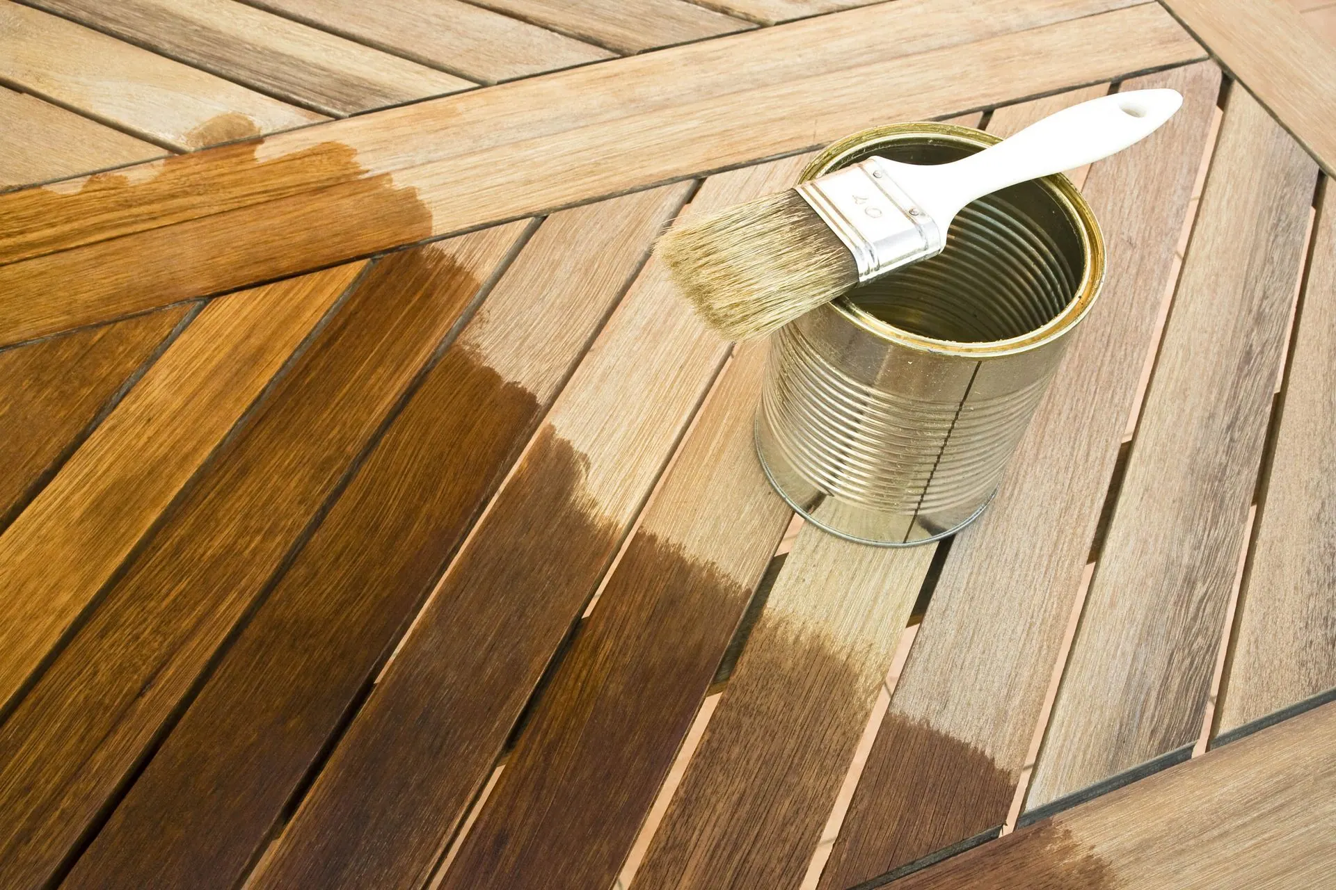 A can of stain and a brush on a wooden deck, half of it freshly stained.